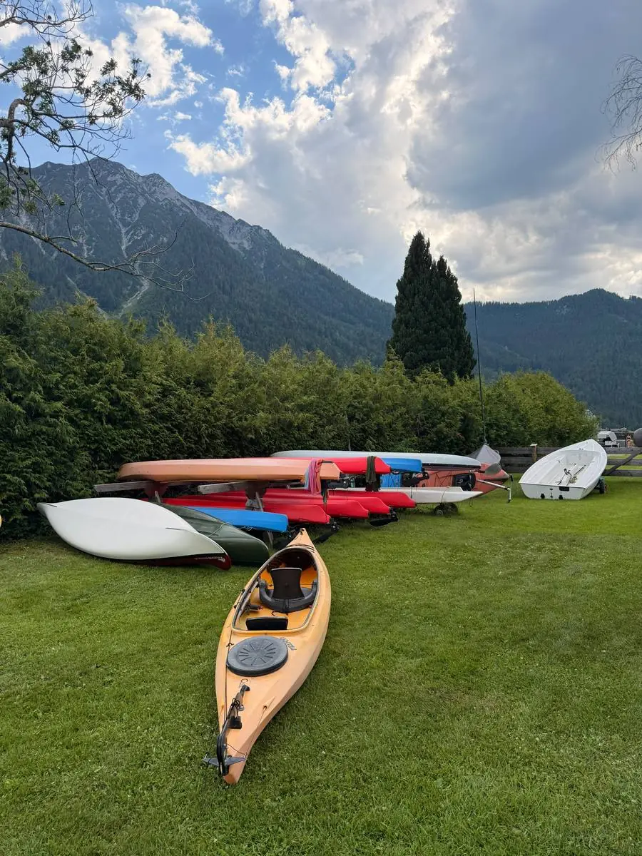 Kajak-Verleih am Achensee: gelbes Kajak auf der Wiese, dahinter Boote und Berge