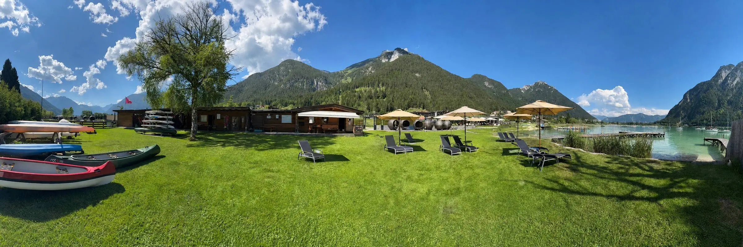 Panorama der Seewiese Buchau: Kanadier, Station und Liegestühle mit Schirmen am Achensee