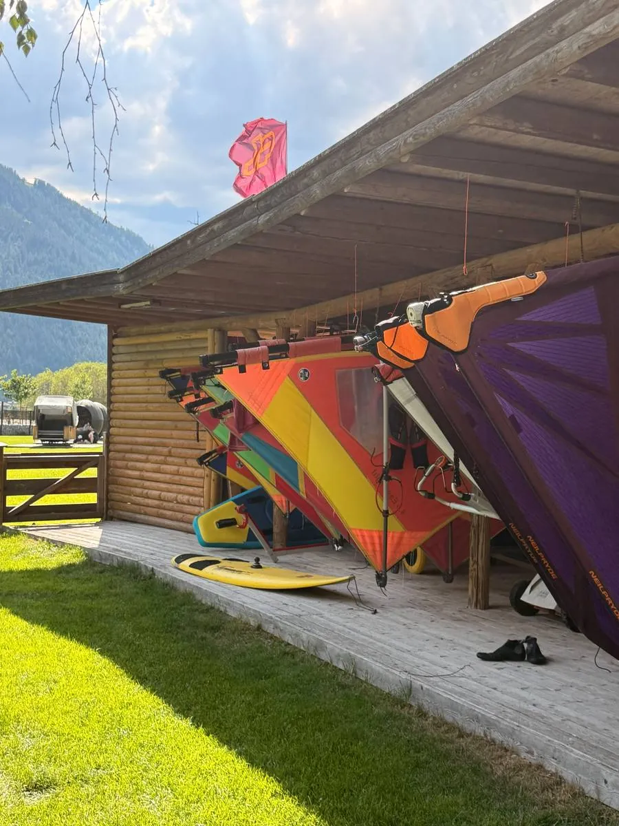 Windsurfkurs am Achensee: bunte Segel aufgeriggt unter dem Holzdach der Station